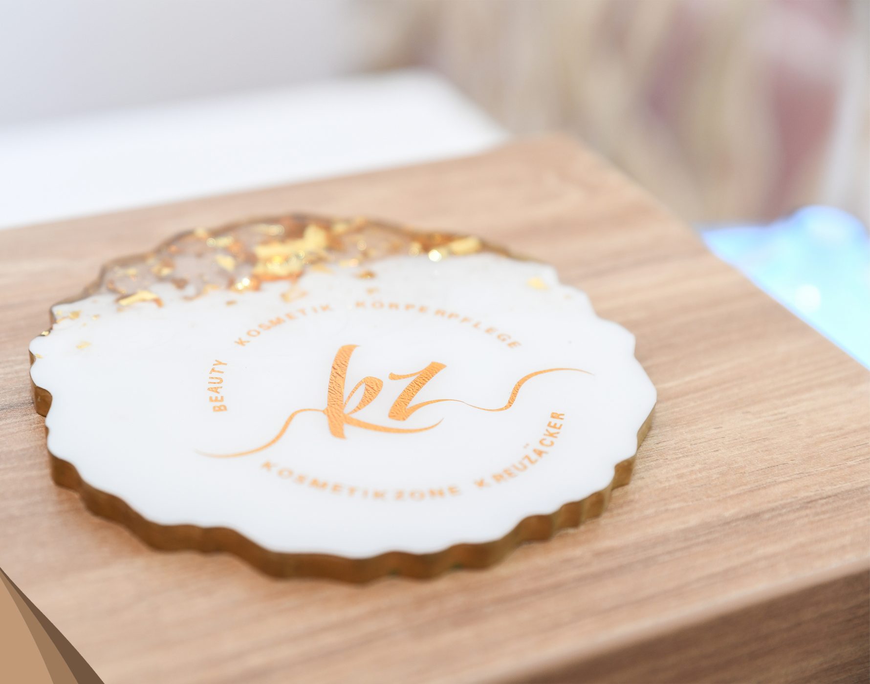 Logo der Kosmetikzone Kreuzäcker in Kupferfolie auf einem Untersetzer aus Kunstharz
